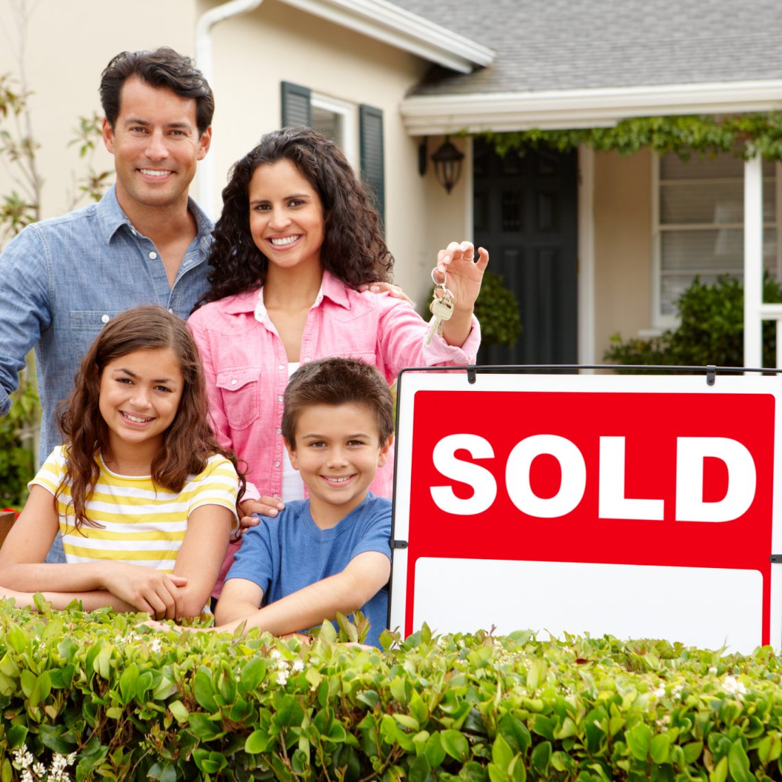 Hispanic family standing outside home smiling with sold sign